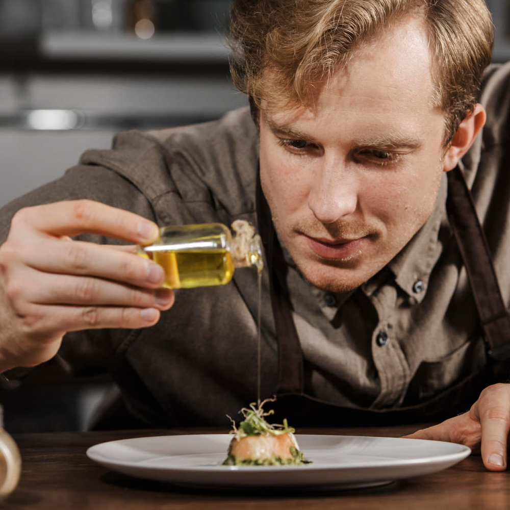 chef joven poniendo aliño a la comida